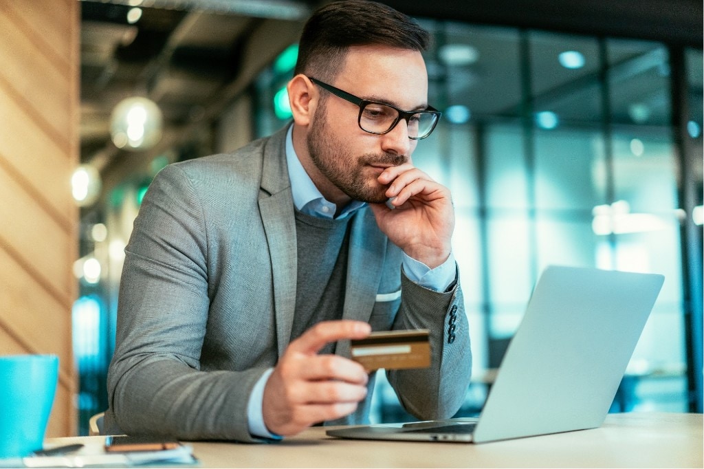 Customer holding a card and completing checkout on a laptop